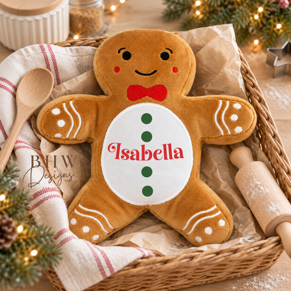 A plush gingerbread person pillow with the name 'Isabella' embroidered on the belly, displayed in a wicker basket with holiday decorations.
