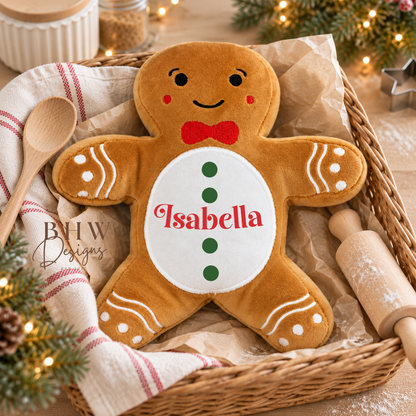 A plush gingerbread person pillow with the name 'Isabella' embroidered on the belly, displayed in a wicker basket with holiday decorations.