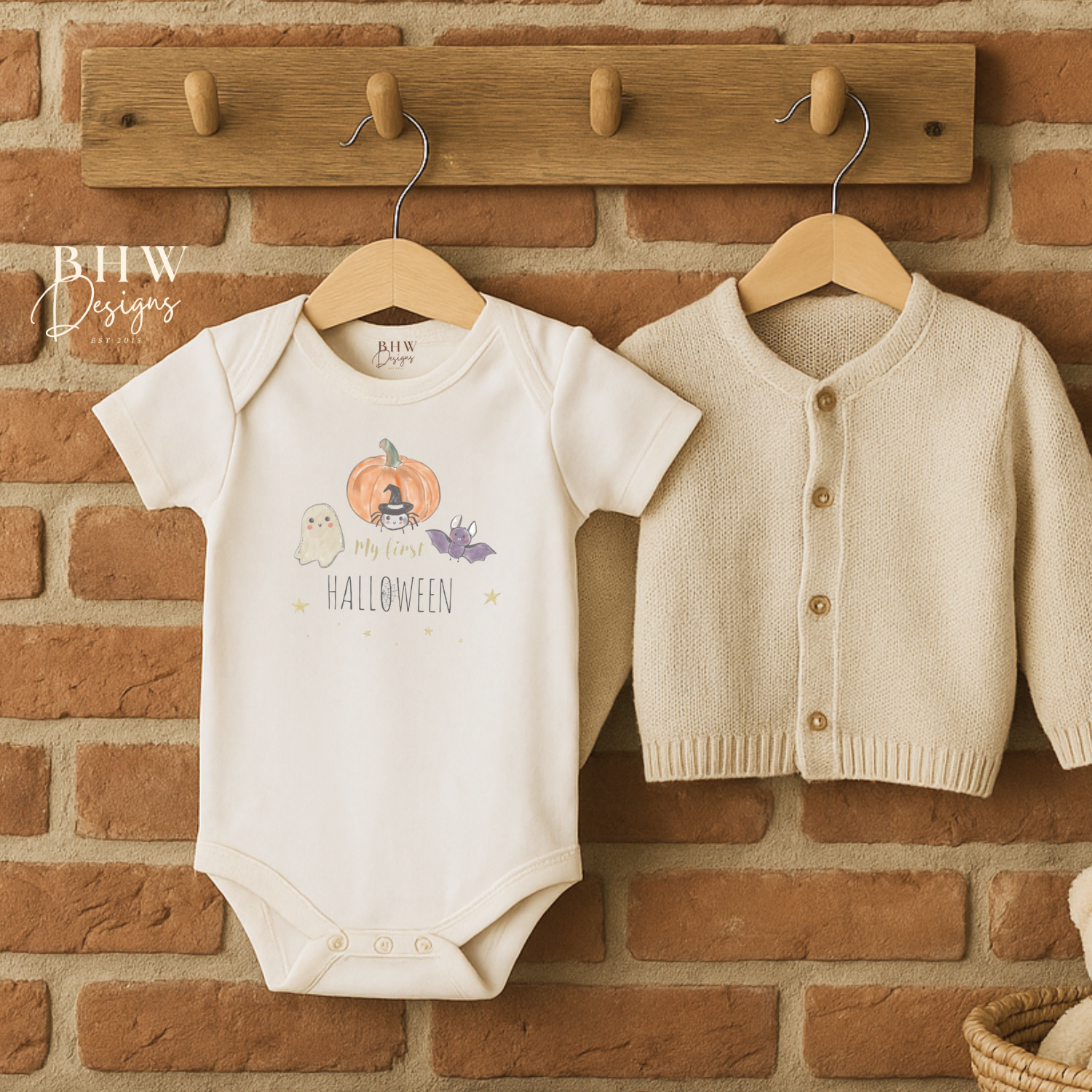 Baby onesie with my first Halloween design and cardigan hanging on a brick wall.