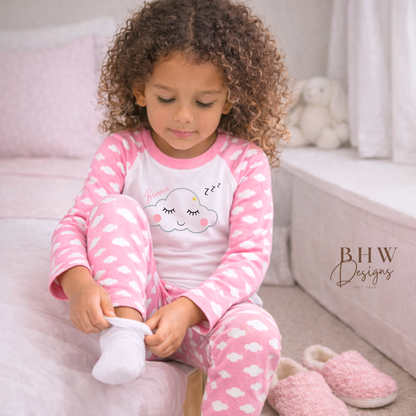 Child wearing pink pyjamas with cloud design, sitting on a bed.