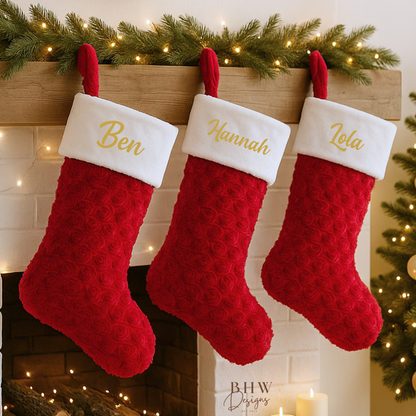 Three red Christmas stockings with names on a fireplace mantle decorated with lights and greenery.