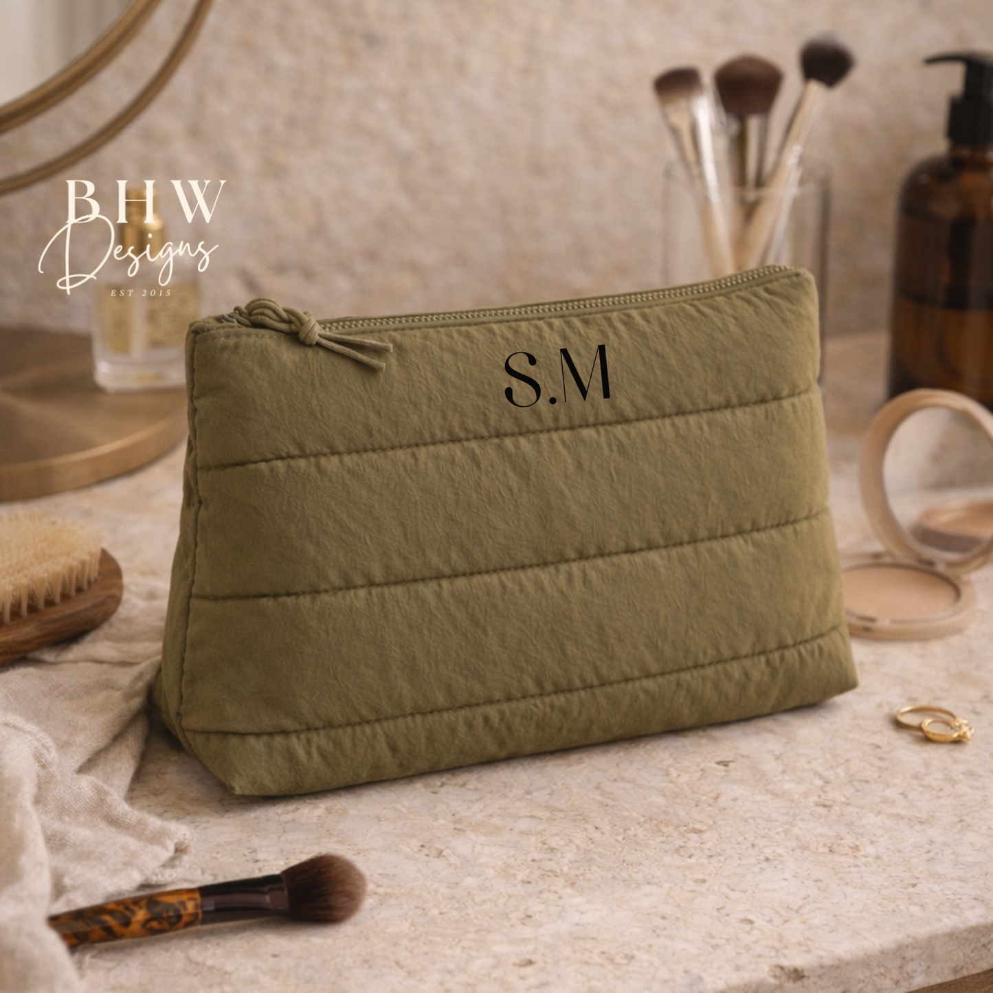 Green cosmetic bag with initials on a vanity table with makeup items.