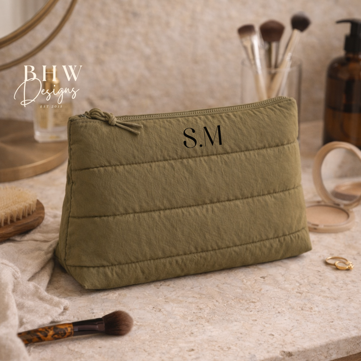 Green cosmetic bag with initials on a vanity table with makeup items.