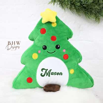 Green plush Christmas tree teddy with a star on top, sitting on a white surface with greenery in the background.
