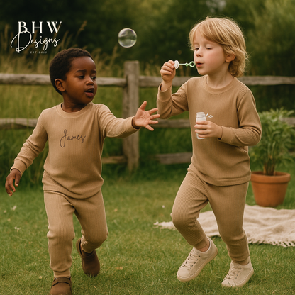 Two children in matching personalised beige ribbed outfits playing with bubbles outdoors.