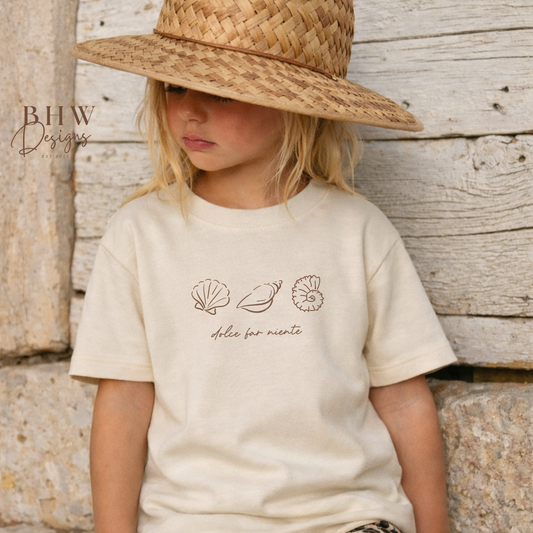 Child wearing a straw hat and a t-shirt with shell designs against a wooden background