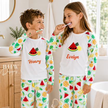 Two children brushing their teeth in matching pyjama's with fruit and watermelon designs, standing in a bathroom.