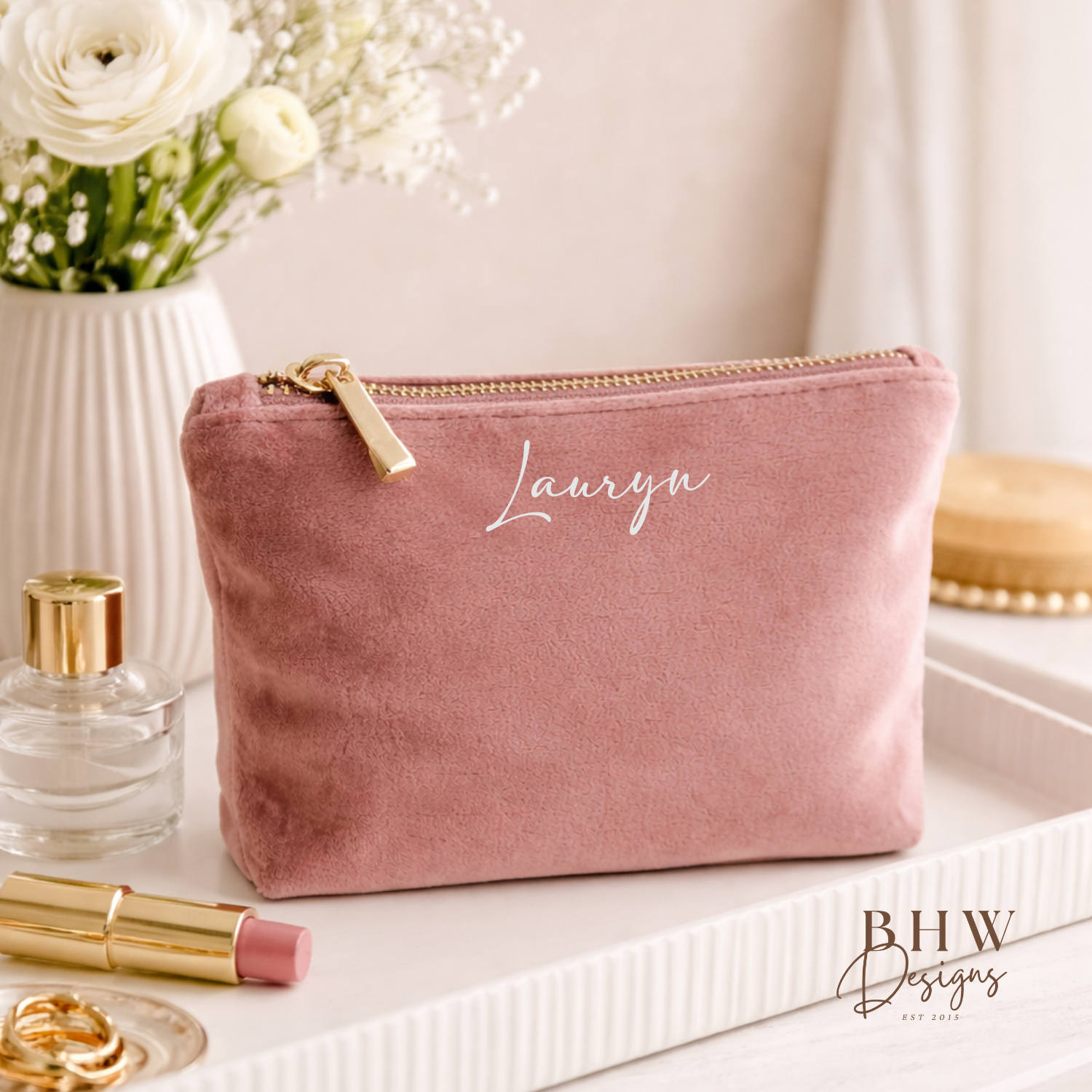 Pink pouch with 'Lauren' branding on a white surface with beauty products and flowers.