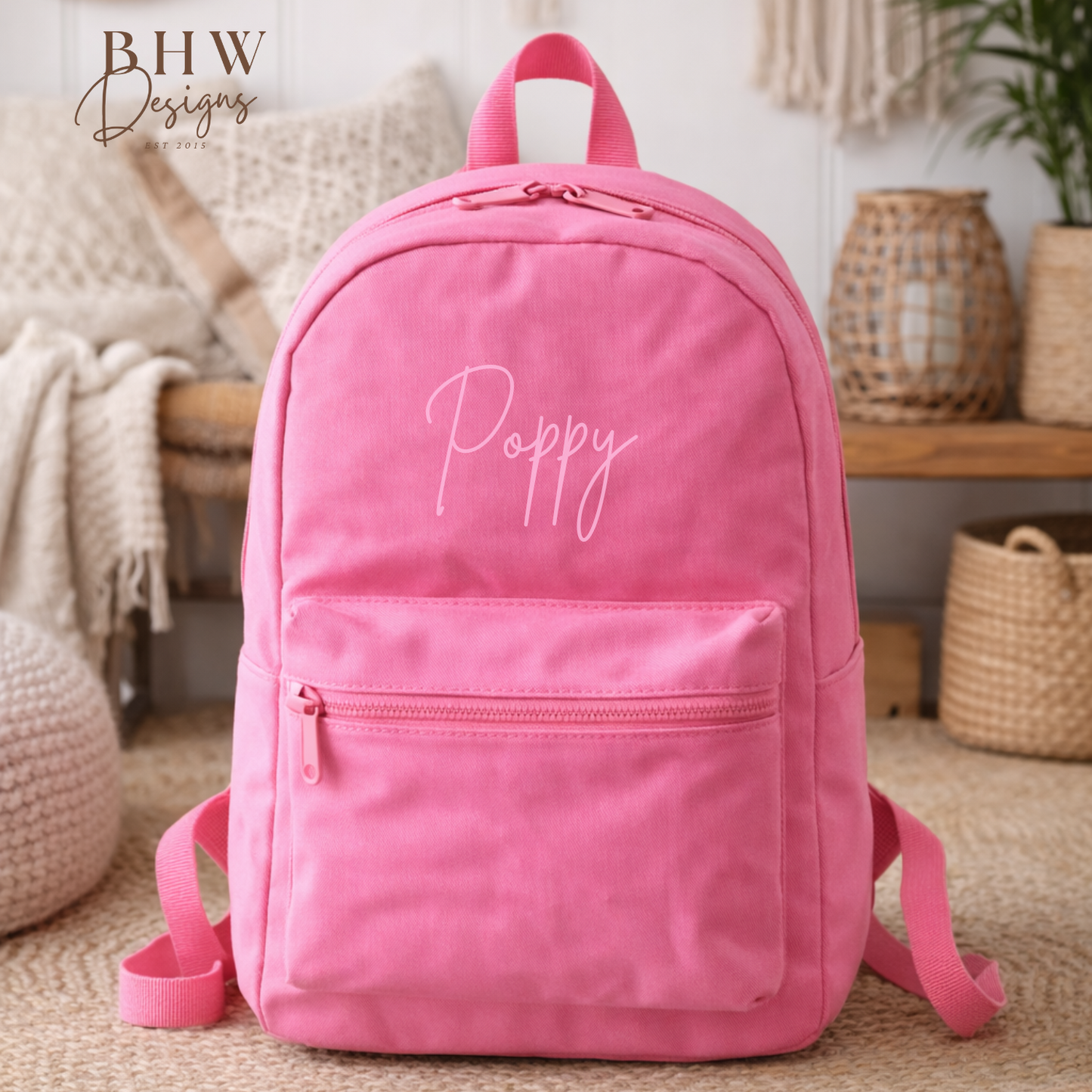 Pink backpack with 'Poppy' embroidery in a home setting