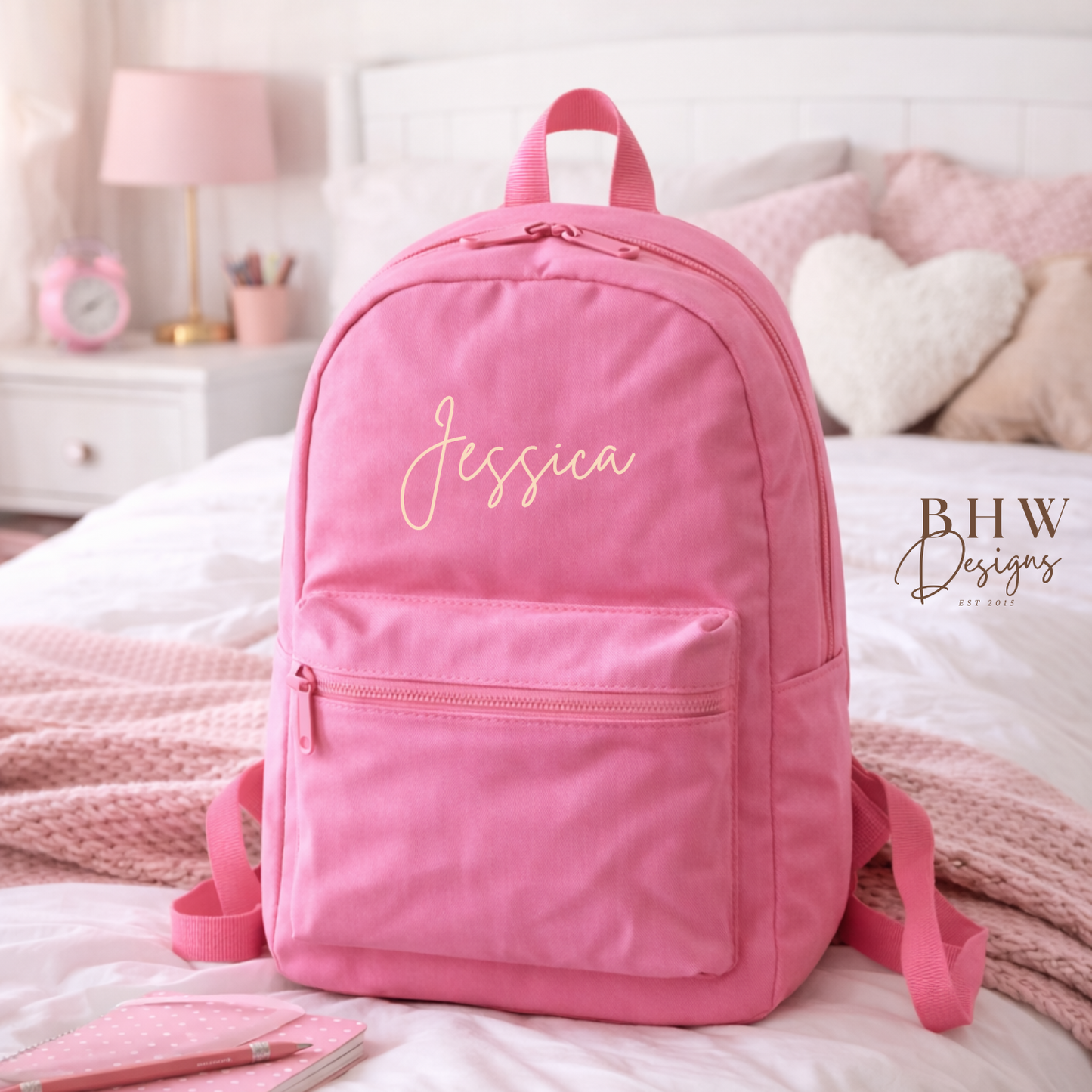 Pink backpack with 'Jessica' printed on it, placed on a bed in a bedroom setting.