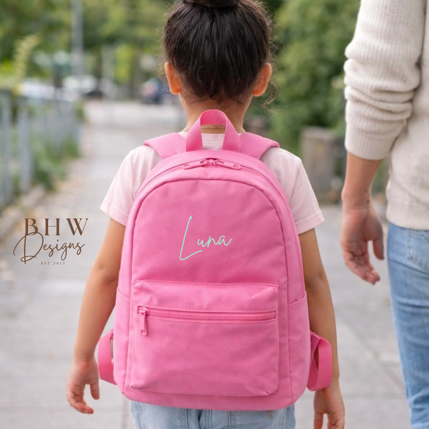 Child wearing a pink backpack with 'Luna' printed on it, walking outdoors.