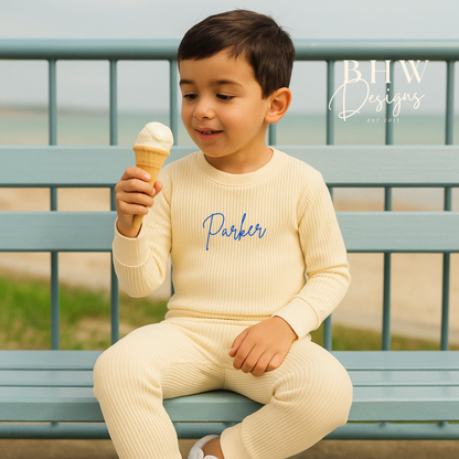 Child wearing a cream outfit with 'Parker' printed on it, sitting on a bench and eating an ice cream.