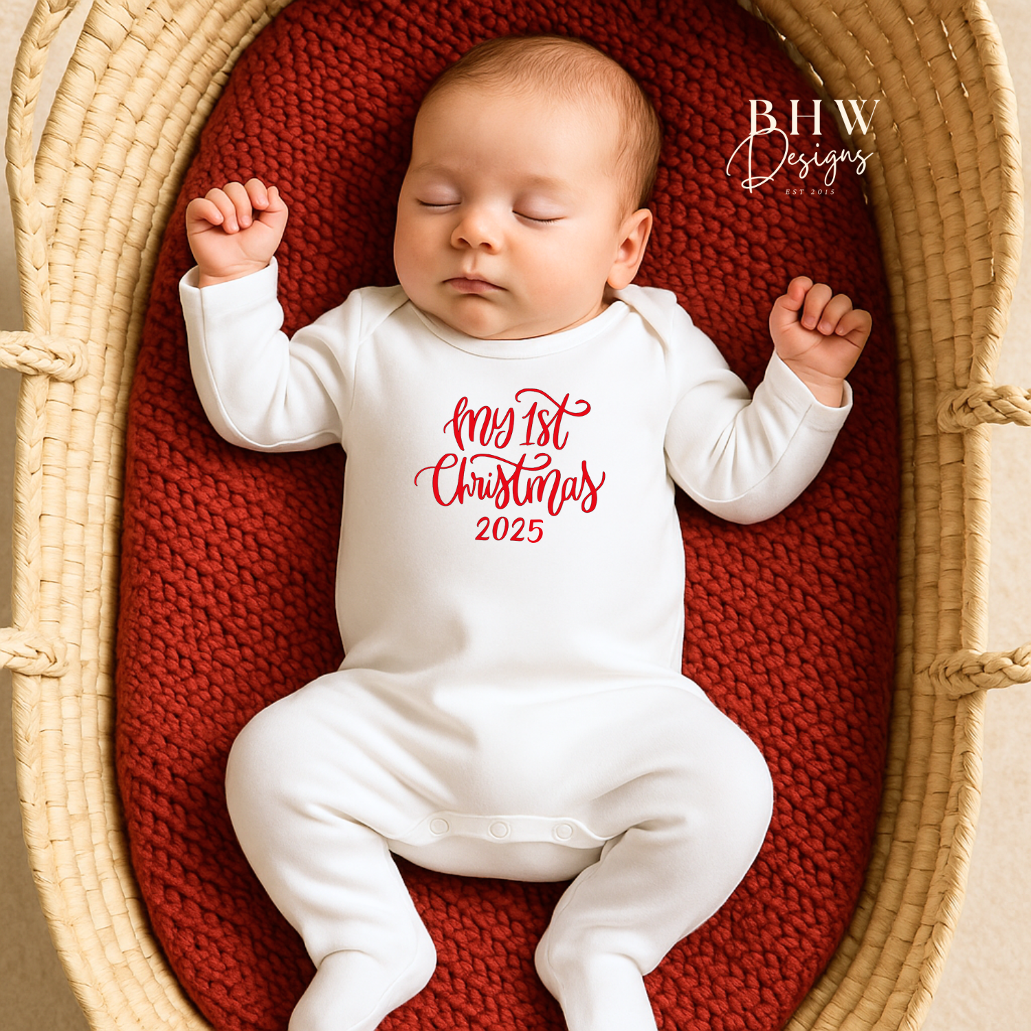 Baby in a white onesie with My First Christmas in red text, lying in a woven basket on a red blanket.