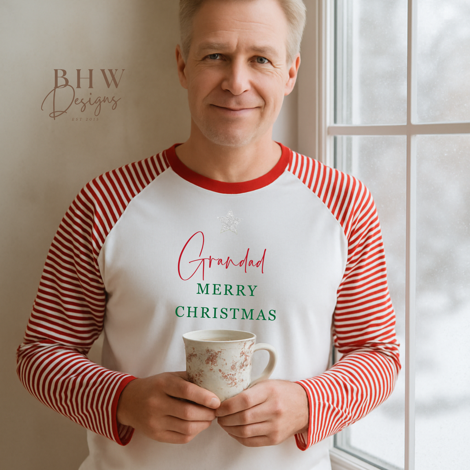 Man wearing red and white stripe pyjamas with 'Grandad Merry Christmas' shirt holding a mug indoors.