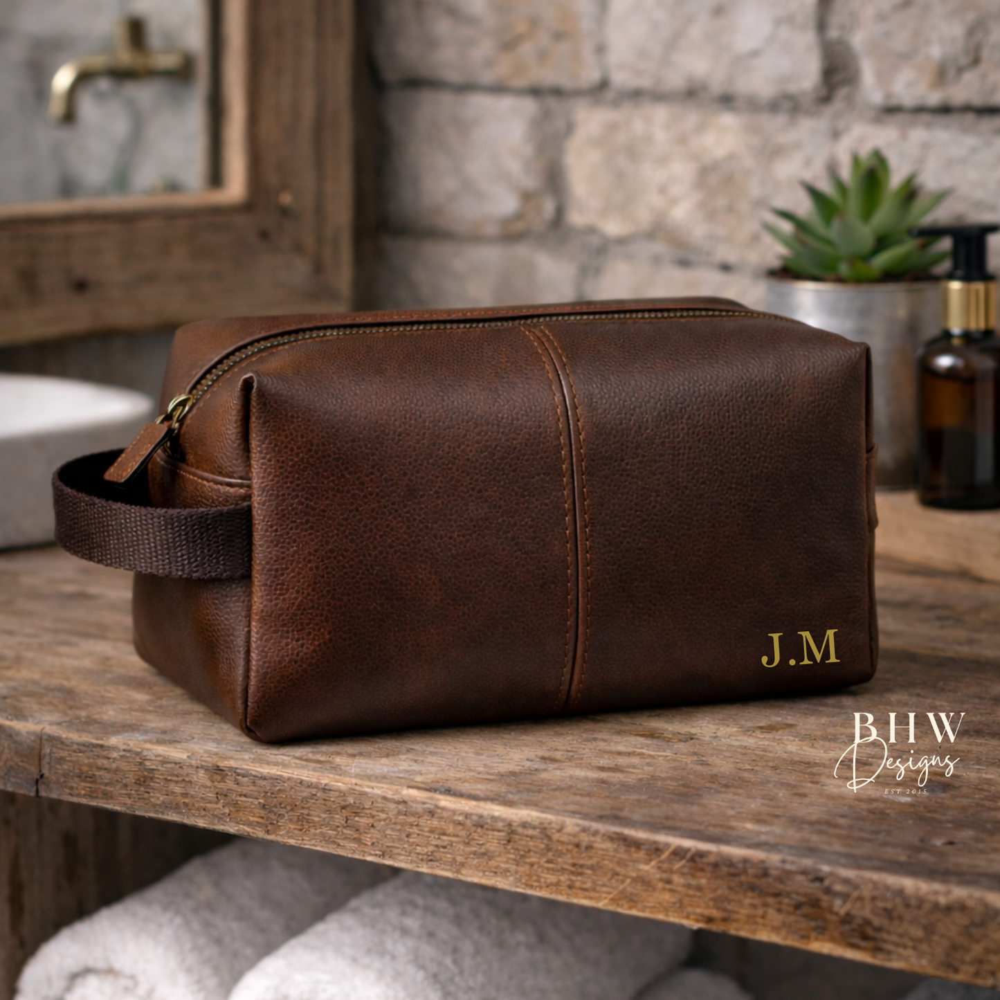 Brown faux leather toiletry bag with initials on a wooden shelf in a bathroom setting.