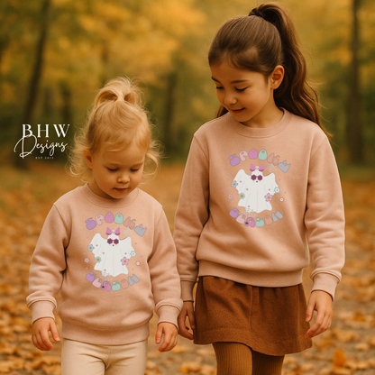 Two children wearing matching blush pink sweatshirts with a spooky season ghost design in an autumn setting.