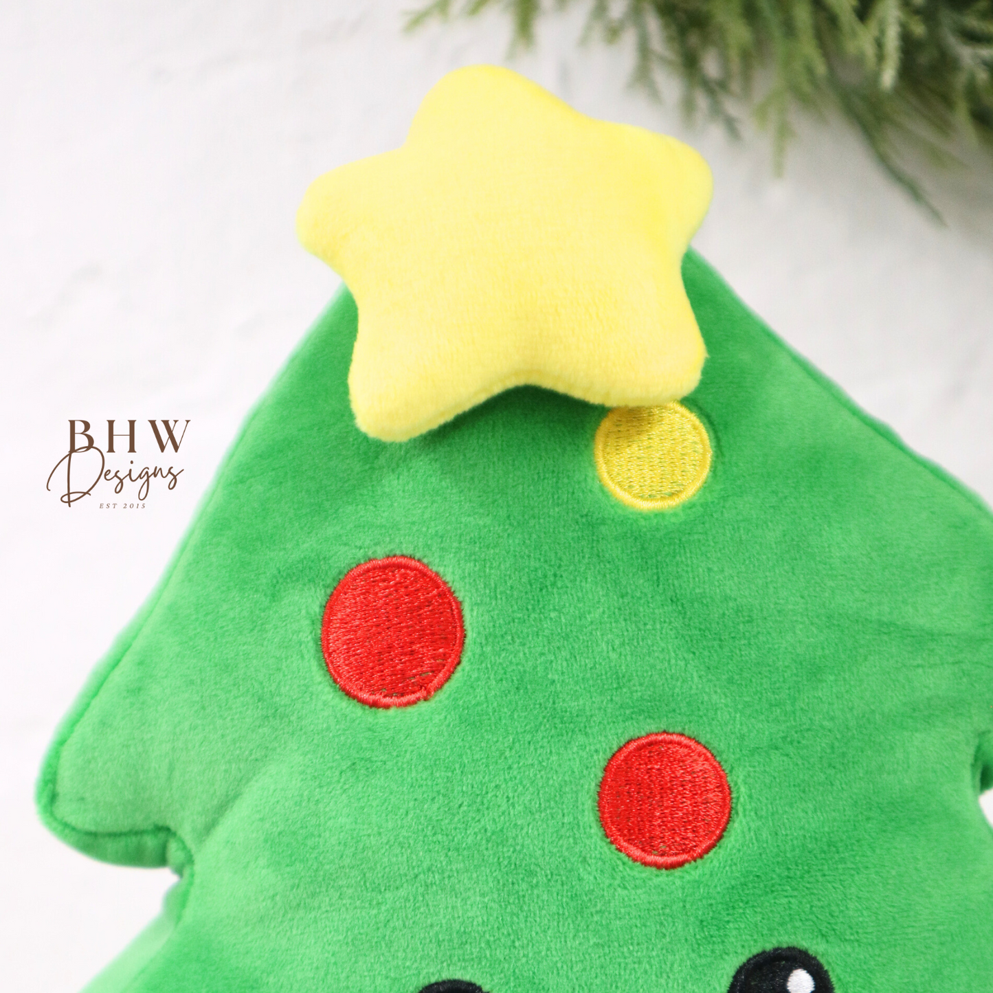 Green plush toy shaped like a Christmas tree with a star on top, red and yellow dots, and a smiley face.