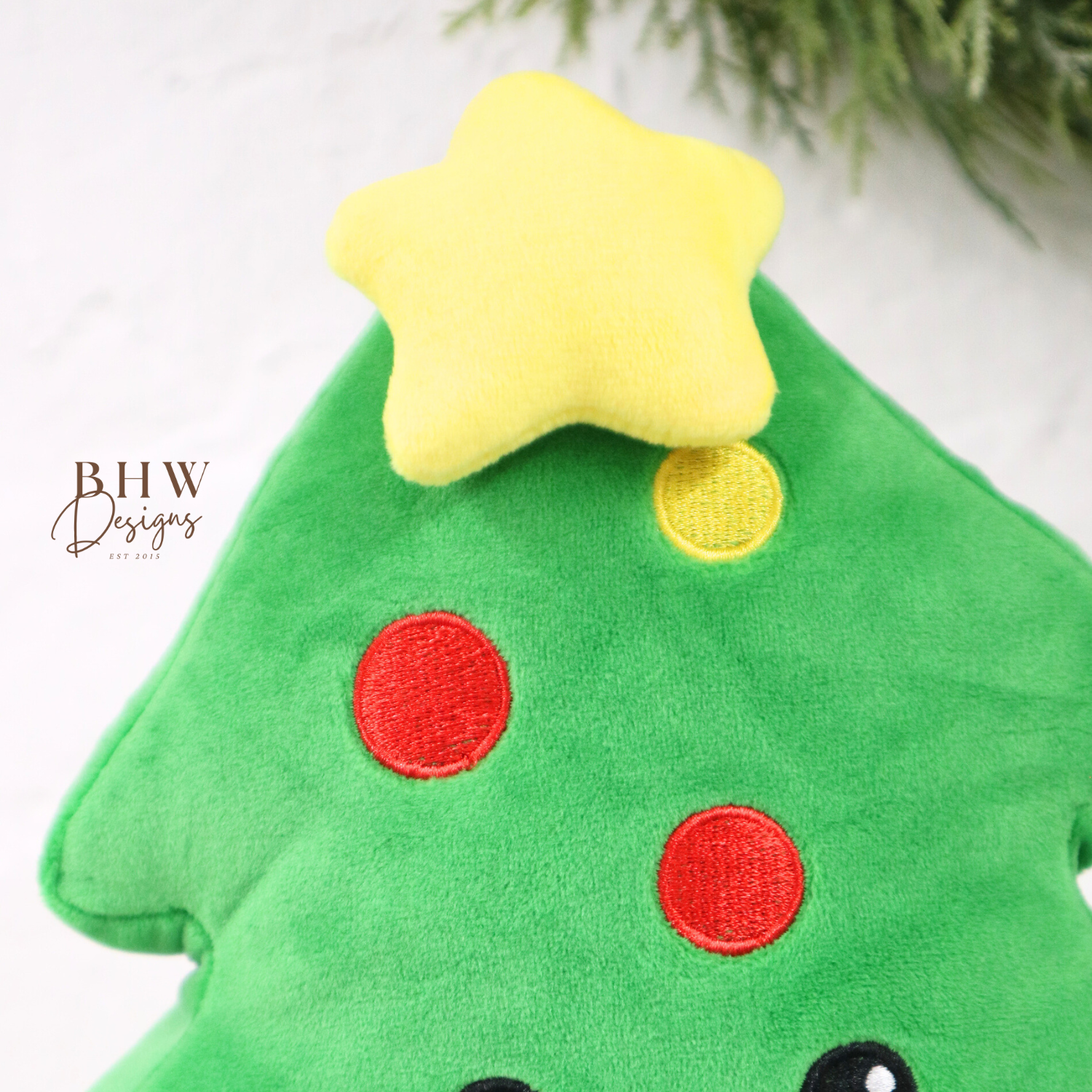 Green plush toy shaped like a Christmas tree with a star on top, red and yellow dots, and a smiley face.