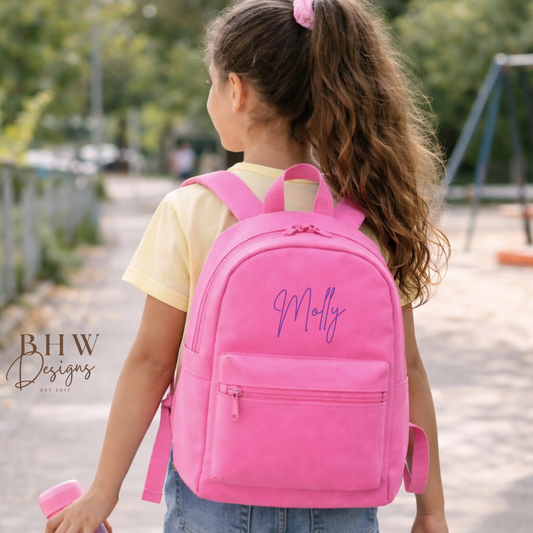 Child wearing a pink backpack with 'Molly' printed on it in purple, standing outdoors.