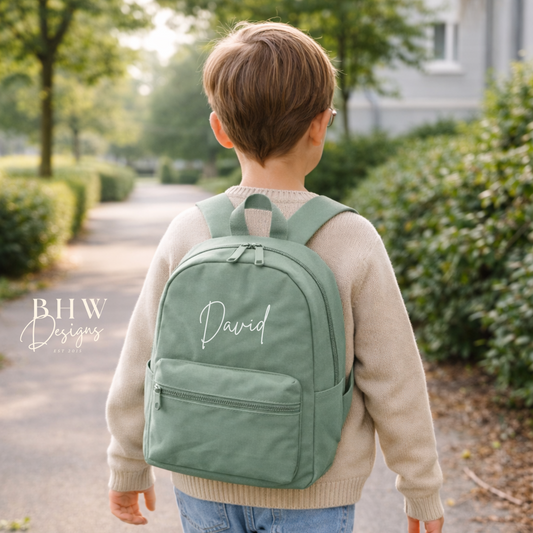 Child wearing a green backpack with 'David' printed on it, standing outdoors.