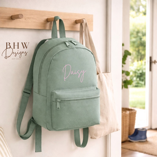 Green backpack with 'Daisy' printed on it hanging on a wooden rack.