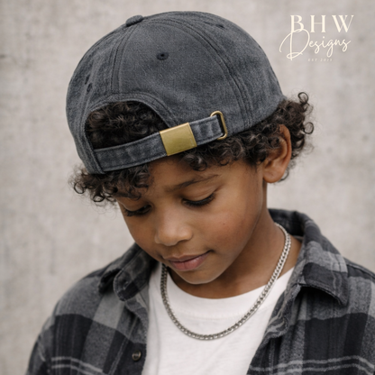 Child wearing a denim cap and plaid shirt against a neutral background