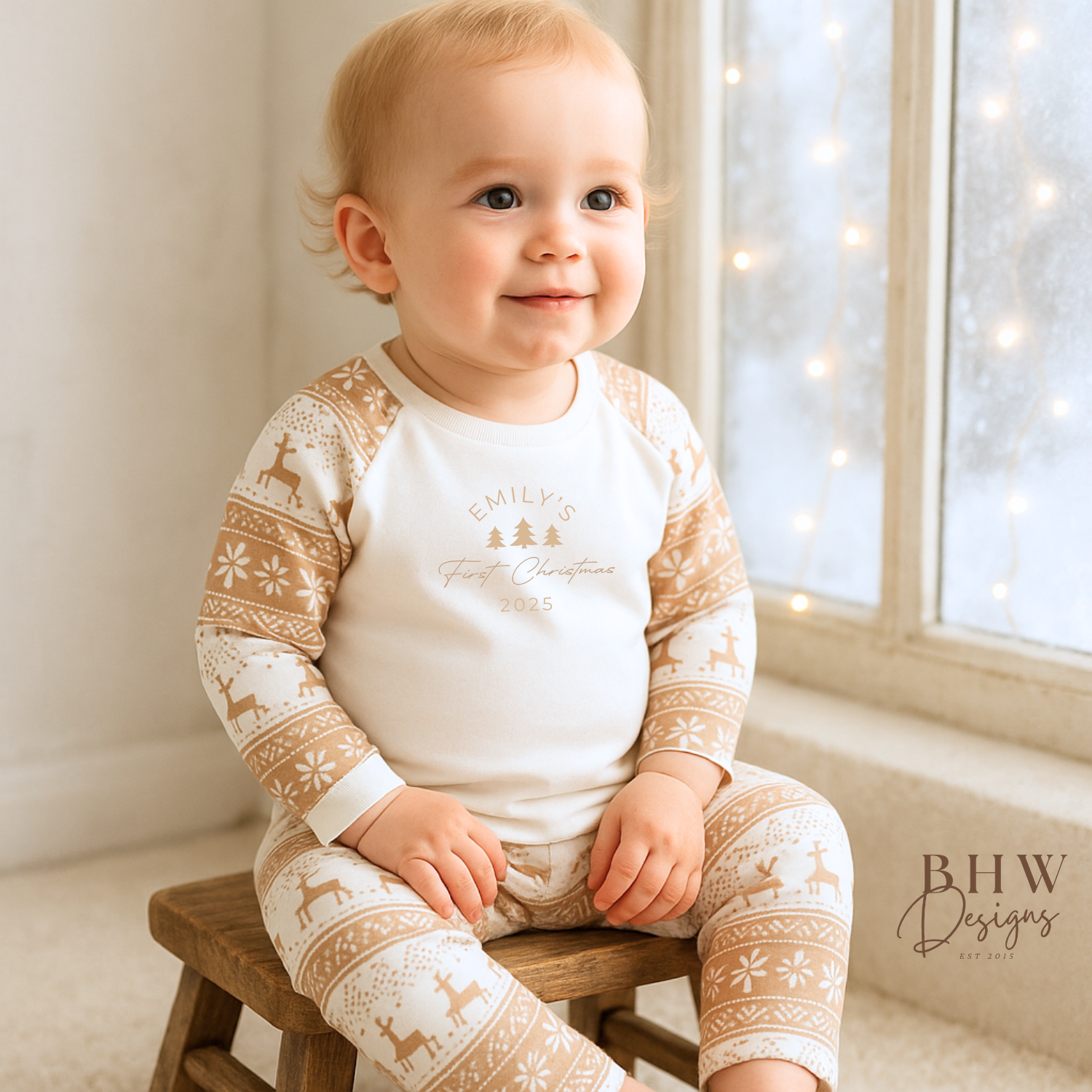 Baby wearing a white and beige fair isle pyjamas with a personalised first Christmas motif on the front.