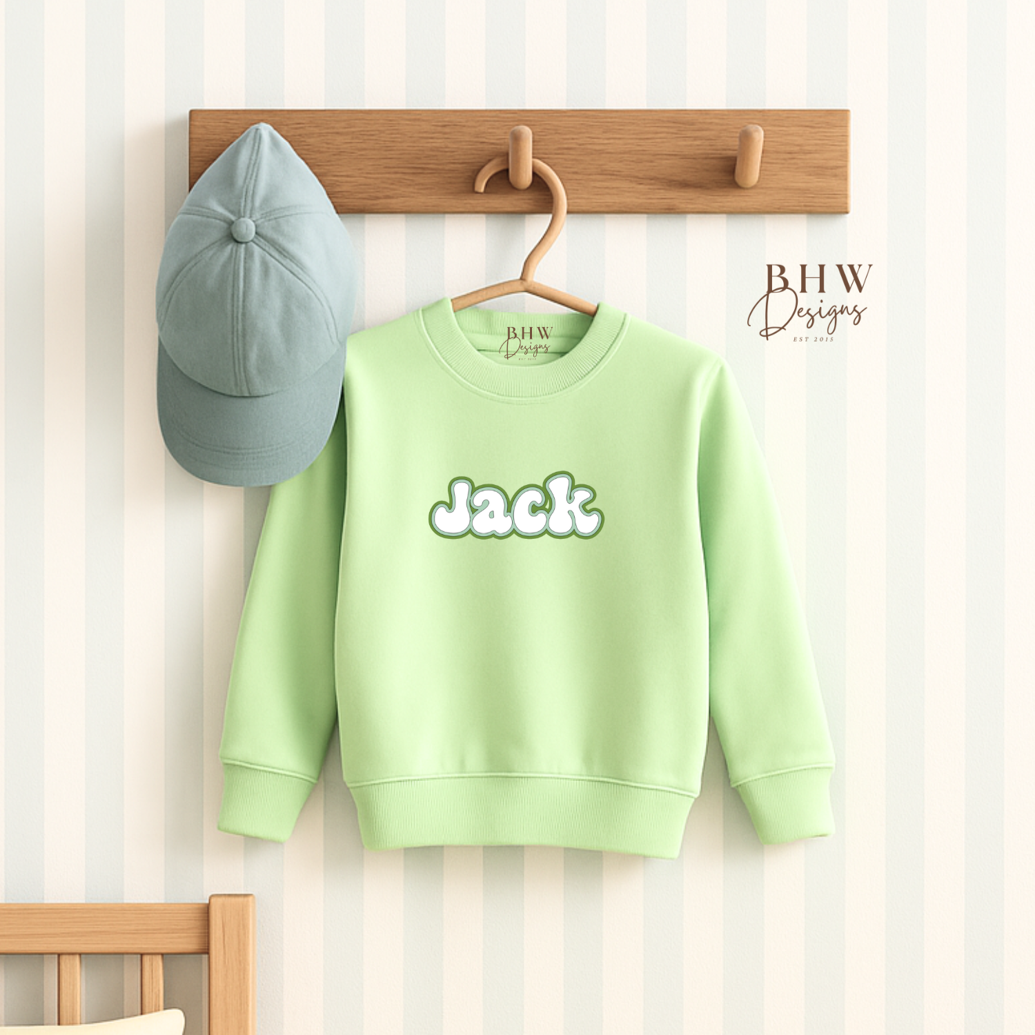 Light green sweatshirt with 'jack' print on a wooden hook against a striped wall.