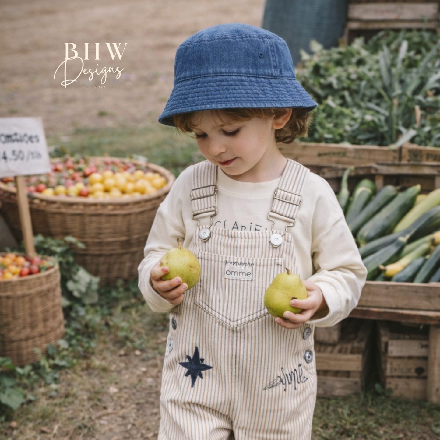 Child in overalls holding apples at a farmers market with with a vintage blue bucket hat