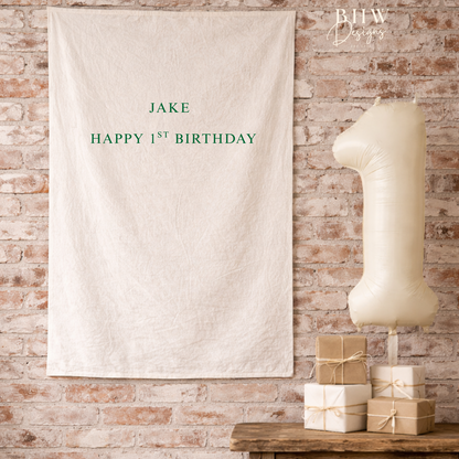 Personalized birthday banner with 'JAKE HAPPY 1ST BIRTHDAY' text on a brick wall background.