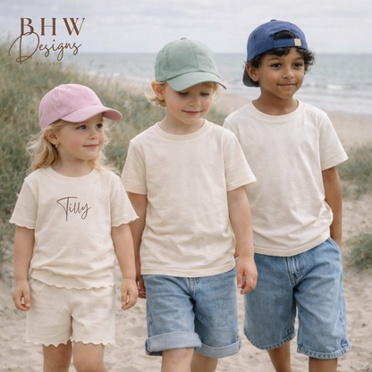 Three children standing on a sandy beach wearing matching outfits with caps
