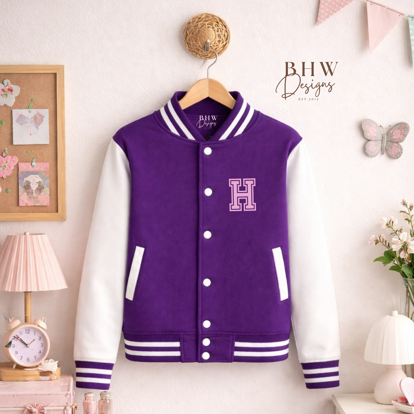 Purple varsity jacket with white accents on a hanger against a wall with decorative items.