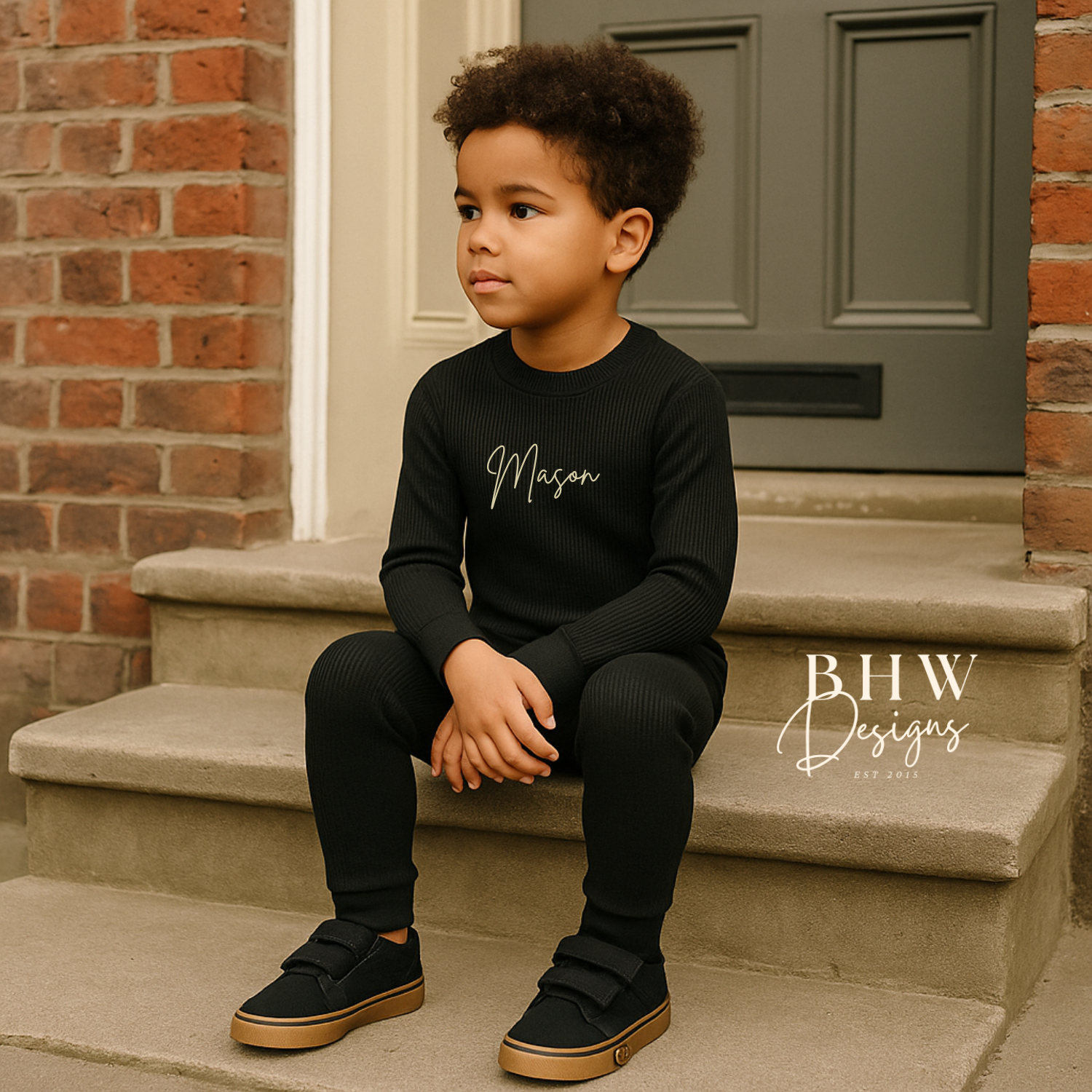 Child sitting on steps wearing a ribbed black outfit with 'Mason' printed on it. 