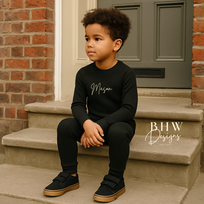 Child sitting on steps wearing a ribbed black outfit with 'Mason' printed on it. 