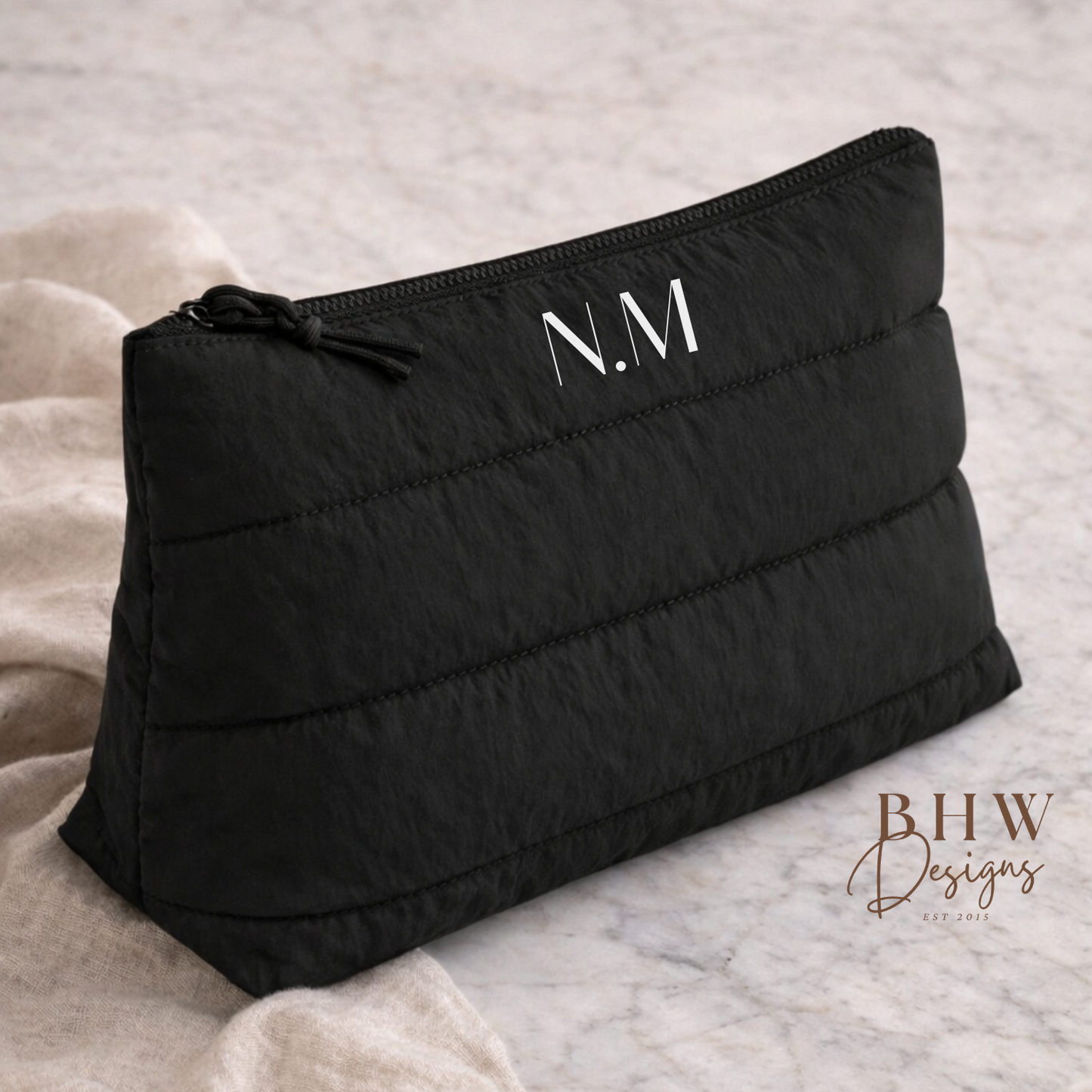 Black quilted pouch with 'N.M.' monogram on a textured surface,
