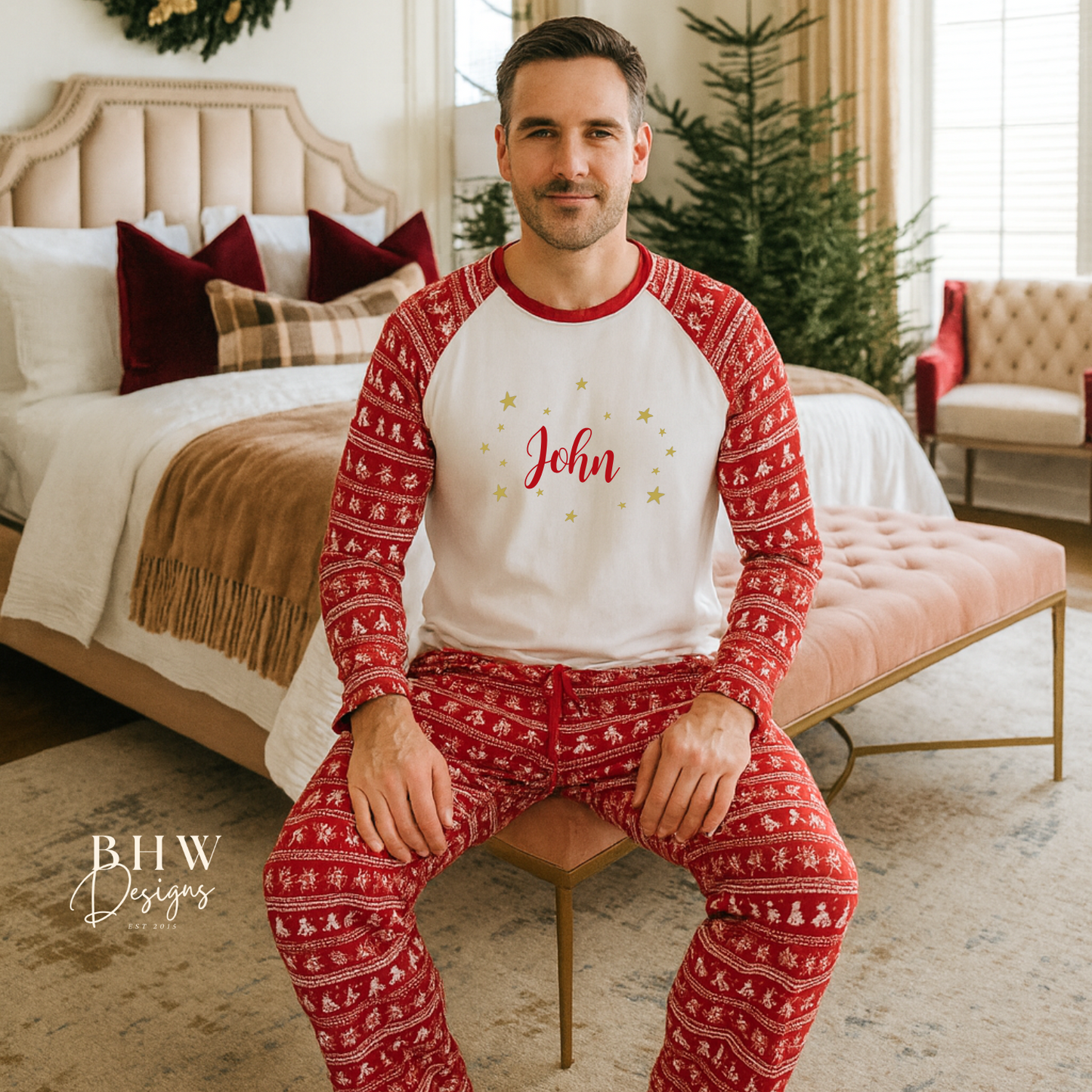 Man wearing red and white Christmas fair isle pyjamas with 'John' printed on them in red adorned by gold stars, sitting in a cozy bedroom.