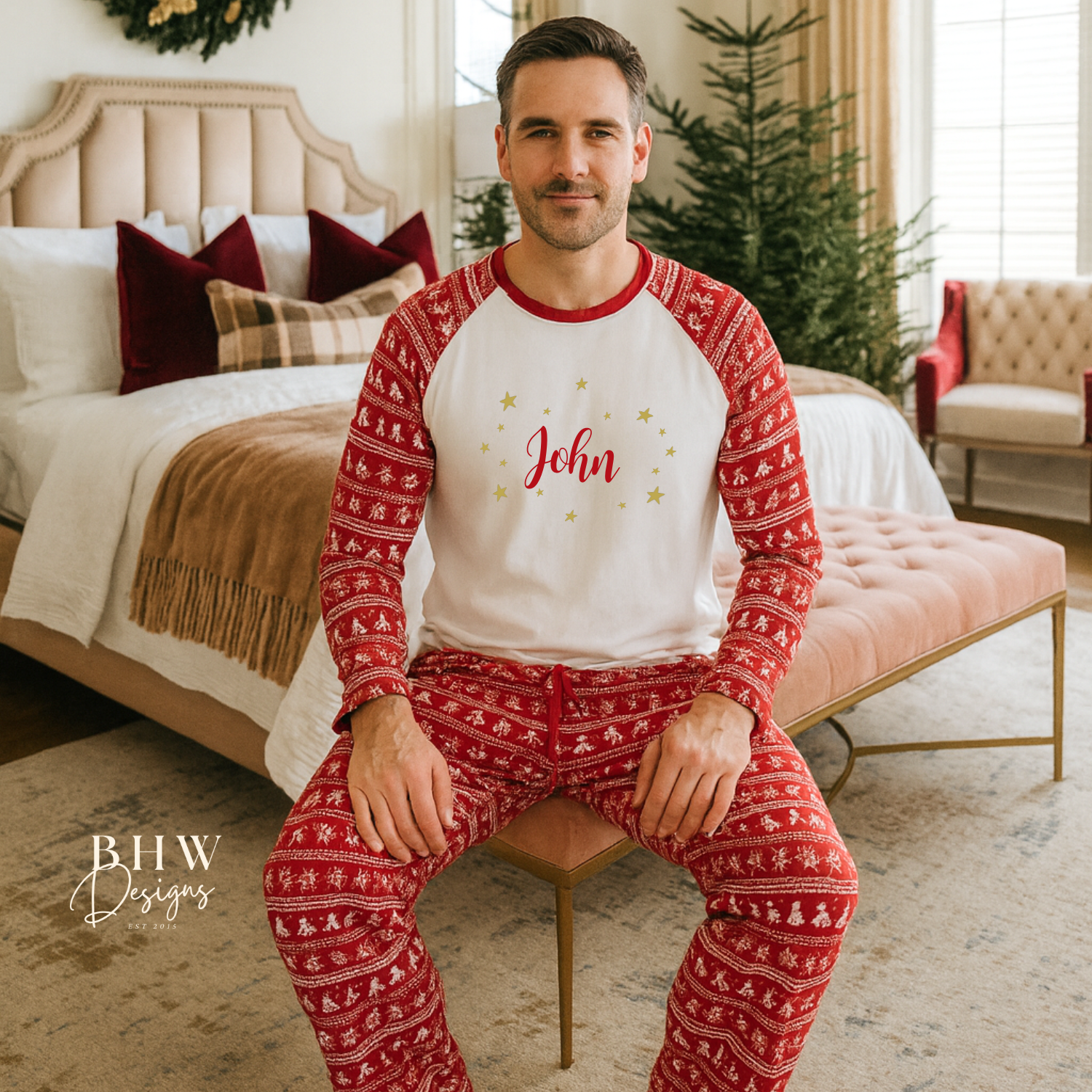 Man wearing red and white Christmas fair isle pyjamas with 'John' printed on them in red adorned by gold stars, sitting in a cozy bedroom.