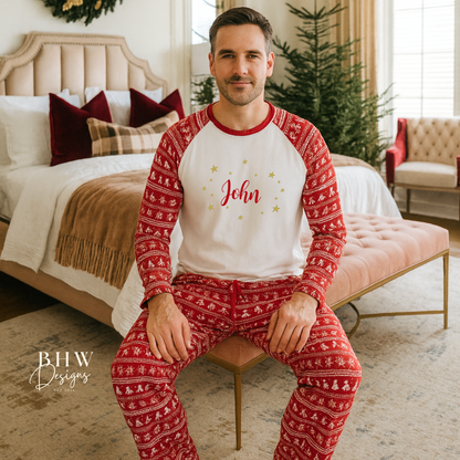 Man wearing red and white Christmas fair isle pyjamas with 'John' printed on them in red adorned by gold stars, sitting in a cozy bedroom.