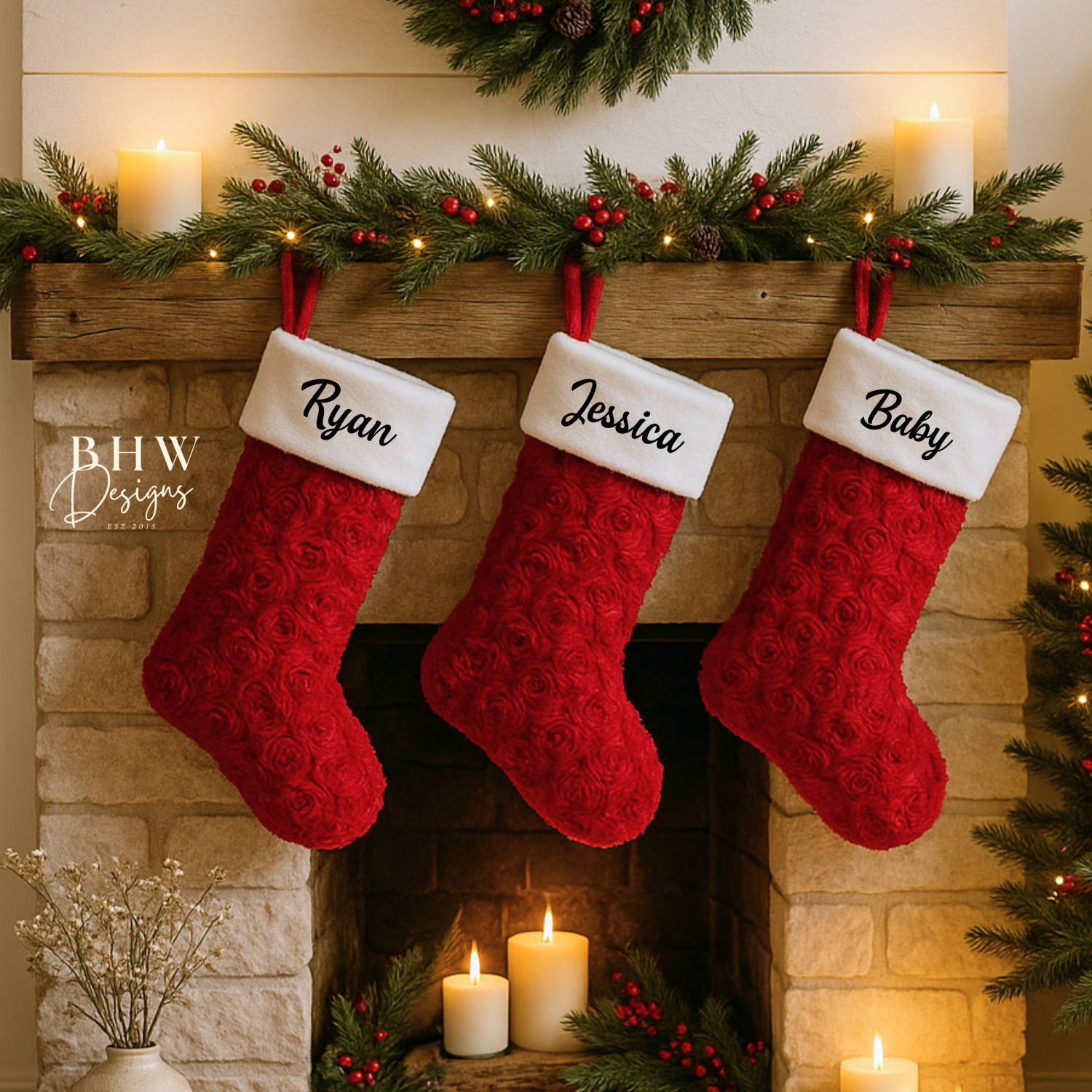 Three red Christmas stockings with names hanging on a fireplace mantle decorated with candles and greenery.