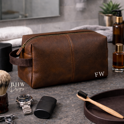 Brown faux leather toiletry bag with initials on a bathroom counter with grooming items.