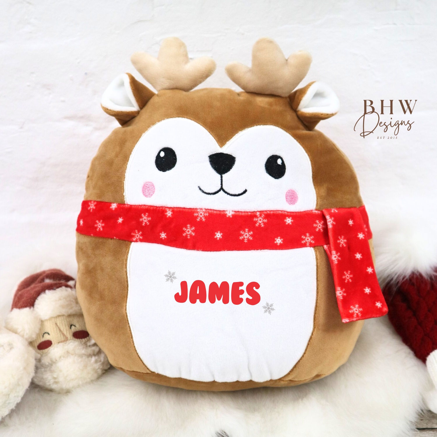 Plush reindeer toy with a red scarf and 'JAMES' text on a snowy background