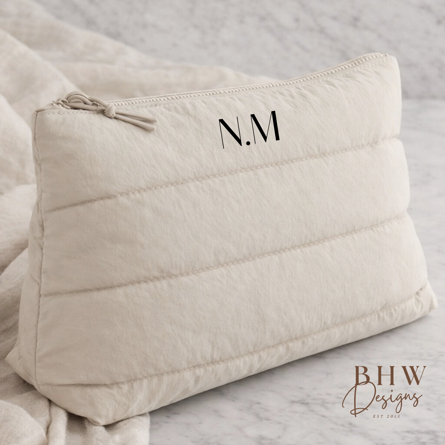 Beige quilted pouch with initials 'N.M.' on a light gray background