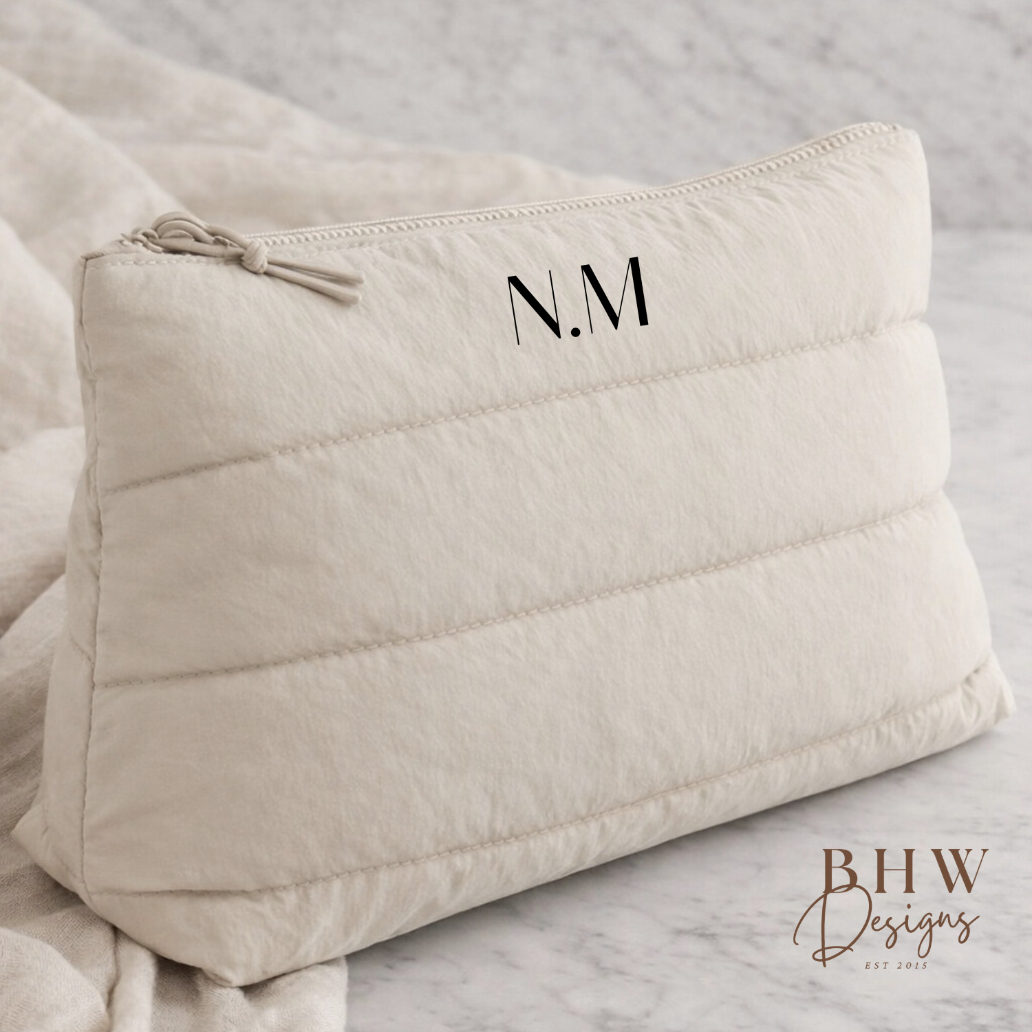 Beige quilted pouch with initials 'N.M.' on a light gray background