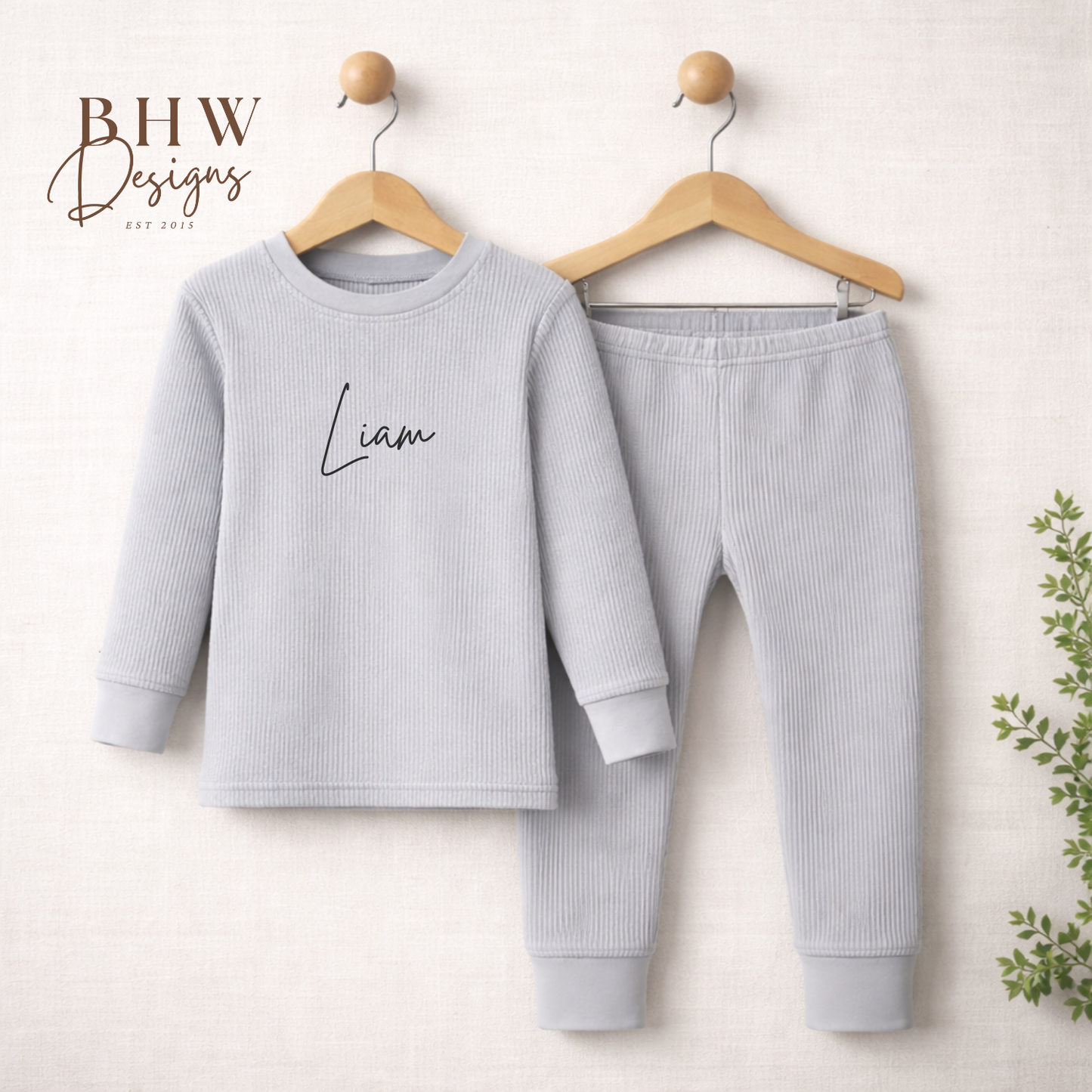 Children's light grey lounge set with 'Liam' on the shirt, hanging on wooden hangers against a white background.