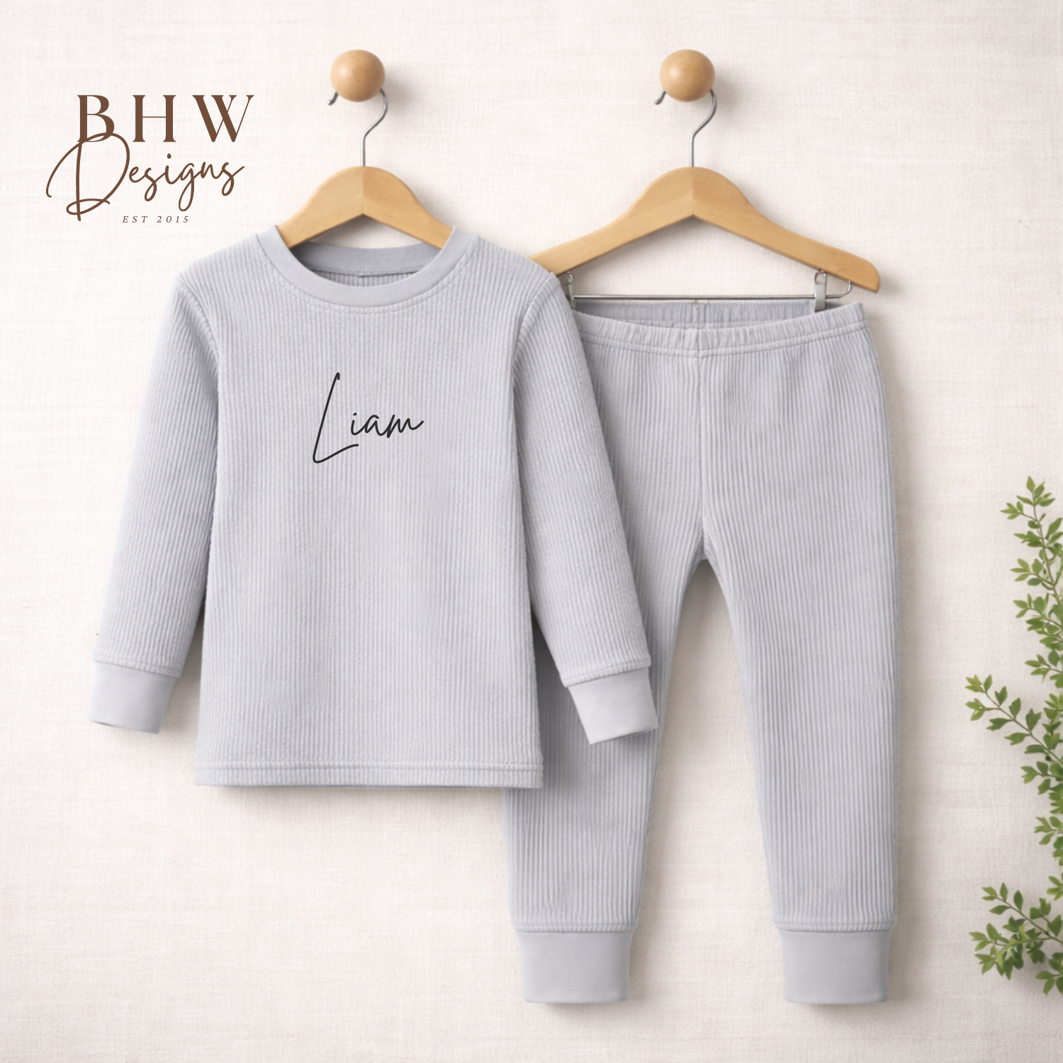 Children's light grey lounge set with 'Liam' on the shirt, hanging on wooden hangers against a white background.