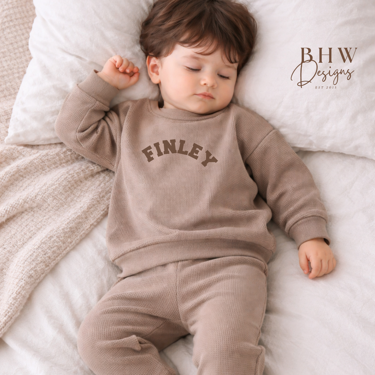 Child wearing a taupe sweatshirt with 'FINLEY' printed on it, lying on a soft surface.