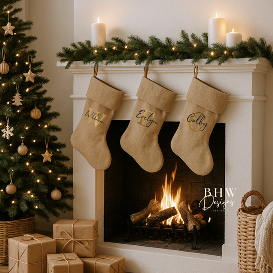Personalised Christmas stockings hanging above a fireplace with a decorated tree and presents on a wooden floor.