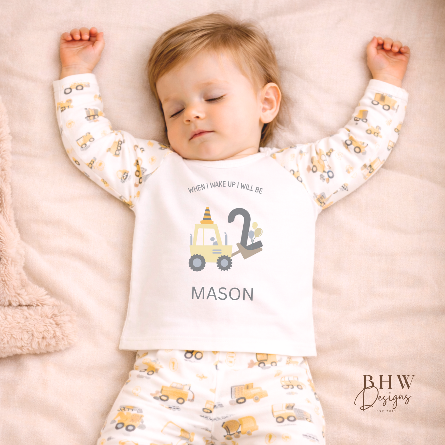 Child wearing personalised pyjamas with construction vehicle design and text, lying on a blanket.
