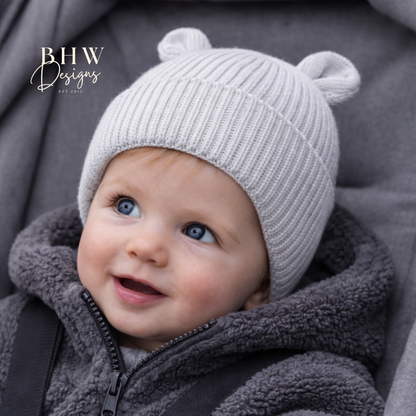 Baby wearing a grey knit hat with bear ears, sitting in a grey car seat.