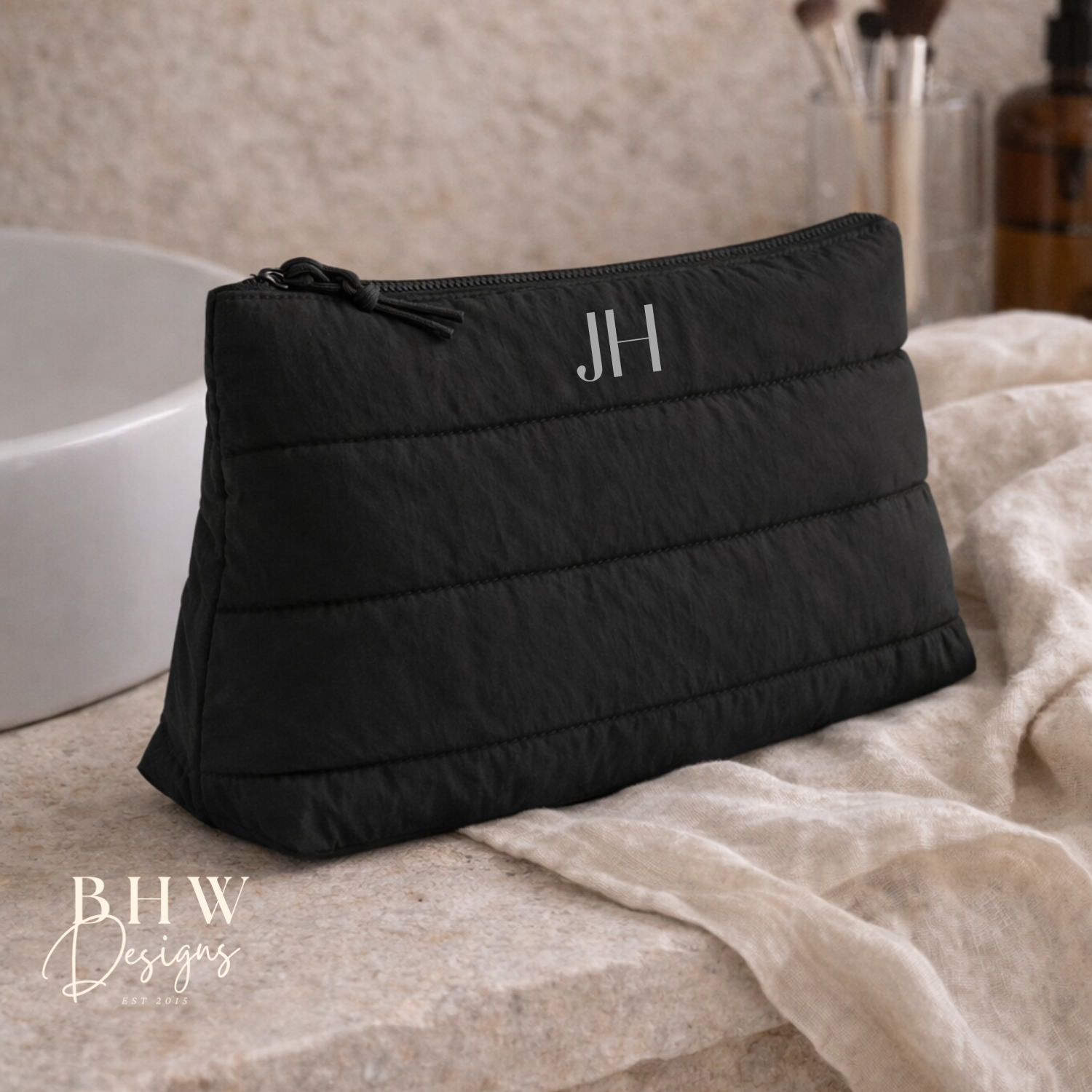 Black quilted pouch with initials on a bathroom counter,